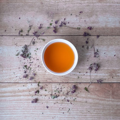 Oregano tea in a white cup on wooden boards. Around the Cup are flowers and leaves of dried oregano.