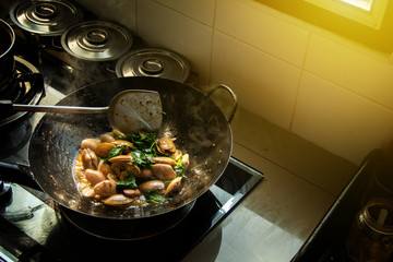 Thai seafood menu Stir Fried Clams with Chili Paste with basil leaves in pan on gas stove with a simple and warm home kitchen atmosphere in the morning.