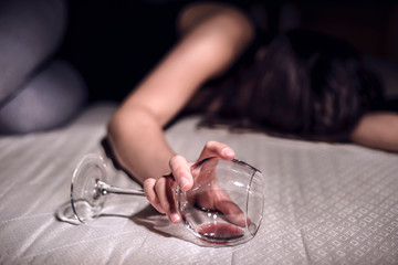 a young girl suffering from chronic alcoholism lies in a dirty room, next to a bottle of wine and a...