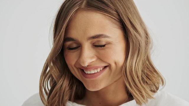 Close up view of flirty smiling young woman wearing basic t-shirt with nose piercing isolated over white background