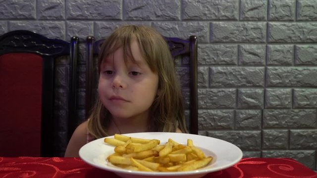 Girl child 5-6 years old eating chips. Charming girl with blond hair eats potatoes.