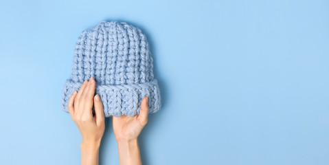 Flat lay fashionable blue knitted winter hat in female hands on blue background top view. Stylish woolen hat, concept of winter accessories for the cold. Advertising, shopping, winter sale