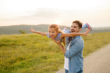 Handsome young father in green sunny summer nature holding his cute small daughter in the arms.