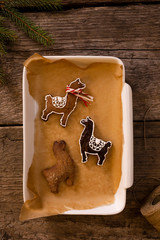 Homemade gingerbread in shapes of lamas packed in a white mold on brown baking paper on old wooden background. © Lukasz