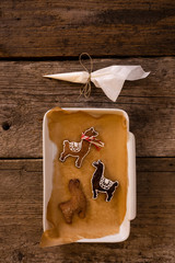 Homemade gingerbread in shapes of lamas packed in a white mold on brown baking paper on old wooden background. © Lukasz