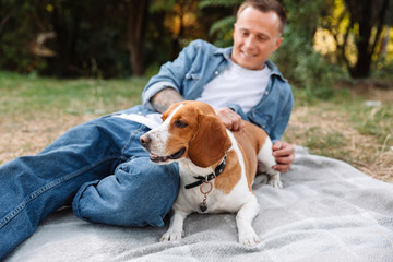 Photo of handsome young man sitting on blanket in park with his canine dog