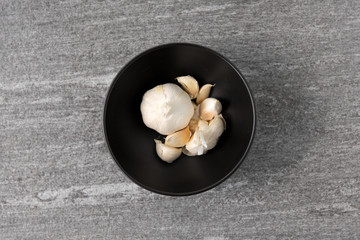 vegetable, food and culinary concept - garlic in bowl on slate stone background