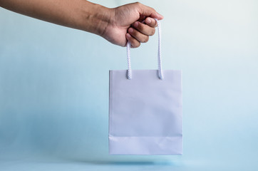 hand holds white paper bag against blue background