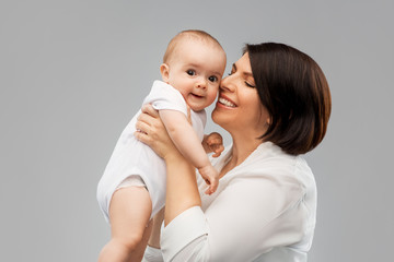 family, child and parenthood concept - happy smiling middle-aged mother holding little baby daughter over grey background