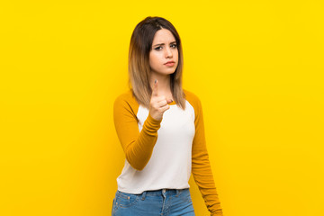 Pretty young woman over isolated yellow wall frustrated and pointing to the front