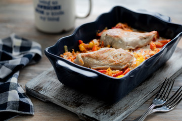 Chicken fillet baked with peppers in a blue ceramic dish on a wooden table