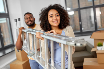 moving, people, repair and real estate concept - happy african american couple with ladder at new...