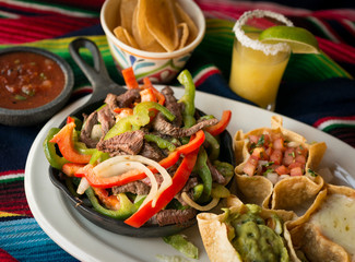 Fajitas with tender skirt beef steak, sautéed bell peppers, onions, tomatoes, in a cast iron skillet. Served with pico de gallo, refried beans, and guacamole in tortilla shells.