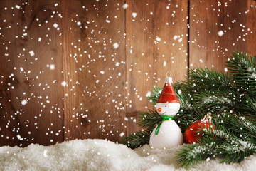 Advent Hintergrund . Eine Schneemann -Baumkugel mit etwas Tanne dekoriert steht vor einer Holzwand im Schnee.