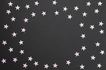 Frame of chaotic numerous pearl confetti in form of small stars on black paper background, copy space. Celebration, holidays, sales, fashion concept. Horizontal. Flatlay. Blank for greeting cards