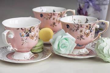 Pink tea cups with floral ornament and macaroon sweets