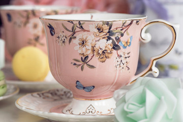 Pink tea cups with floral ornament and macaroon sweets
