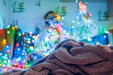 winter holidays preparing cozy domestic atmosphere lonely girl unfocused silhouette background happy emotion with garland unfocused colorful light illumination, blanket texture foreground 