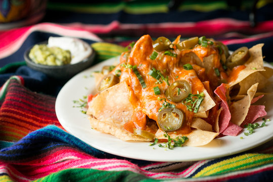 Nachos with melted cheese, beans, guacamole, sour cream, salsa, green onions, jalape&ntilde;os, and enchilada sauce. Presented on a mexican sarape.