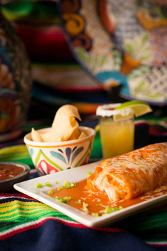 Burrito covered in enchilada sauce and melted cheese served with nachos and salsa.