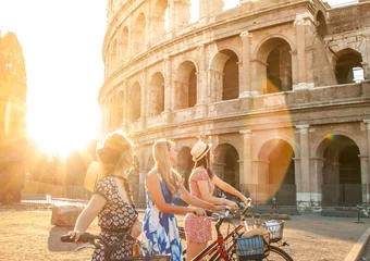Photo sur Plexiglas Rome Trois jeunes femmes heureuses amis touristes avec des vélos au Colisée à Rome, Italie au lever du soleil.