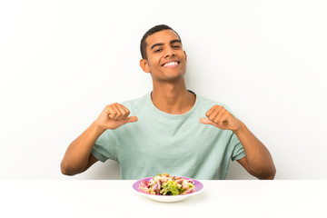Young handsome man with salad in a table proud and self-satisfied