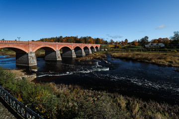 Fototapeta premium Daytime view of historic red brick bridge over river Venta in Europe-Latvia-Kuldīga.