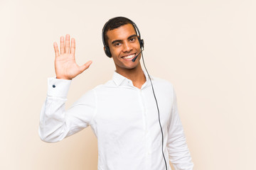 Young brunette man working with a headset saluting with hand with happy expression