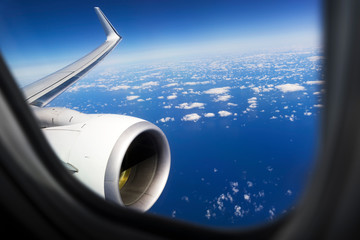 commercial airplane window with plane wing, engine, blue sky and clouds