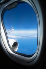 Fototapeta premium commercial airplane window with plane wing, engine, blue sky and clouds