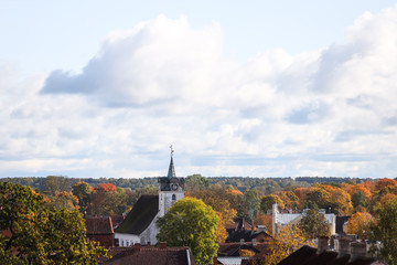 Fototapeta premium Widok z dachu małego wiejskiego miasta na stary biały kościół jako główny temat. Zdjęcie zrobione na Łotwie-Kuldīga w słoneczny jesienny dzień.