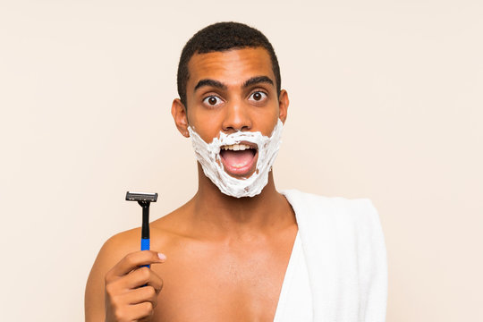 Young handsome man shaving his beard over isolated background with surprise and shocked facial expression
