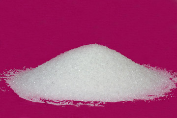 Heap of white granulated sugar on a pink background