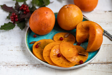Persimmon on a light, wooden background. Near walnuts, viburnum berries. Winter fruit. Healthy eating Orange color. Copy space. 