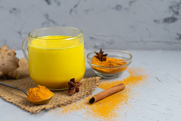 Healthy turmeric drink with latte milk in a glass glass. Golden milk with turmeric, ginger root, cinnamon stick and honey on a dark background. Detox tea. Healthy eating Copy space. 