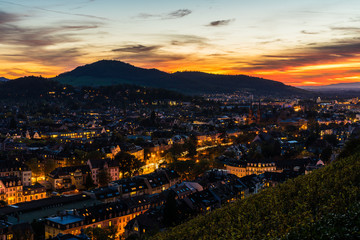 Fototapeta na wymiar Germany, Freiburg im breisgau city skyline, cityscape and houses illuminated by night, decorated by magical red sunset sky, aerial view above roofs