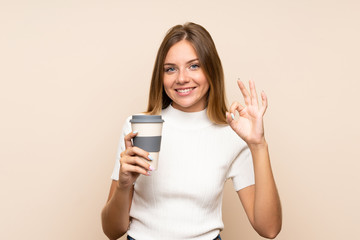 Fototapeta premium Young blonde woman over isolated background holding coffee to take away while making OK sign
