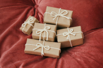Presents for a Christmas. Gift boxes wrapped in craft paper and tie white string. Red velvet cloth background. Holiday mood.