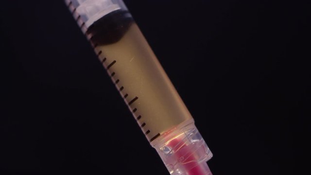 Liquid brown heroin and blood getting sucked into a syringe from a needle