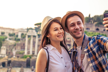 Young couple tourist looking at Roman Forum at sunrise and taking selfie. Historical imperial Foro Romano in Rome, Italy from panoramic point of view.