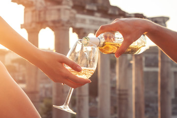 Pouring bottle of white wine in glasses at Roman Forum at sunrise. Historical imperial Foro Romano...