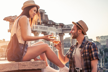 Young couple tourist with glass of white wine at Roman Forum at sunrise. Historical imperial Foro...