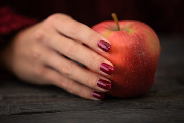Close up photo of a woman holding red apple in a hand above black wooden table.
