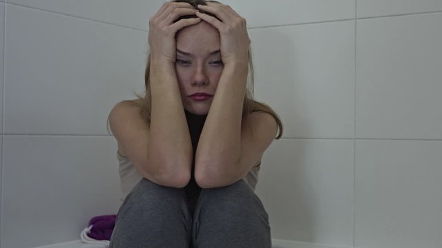 Depressed woman alone inside a bathroom. Sad brunette girl expresses anxiety issue and thinking deeply because of personal problems ideal for women abuse awareness campaign or relationship break up