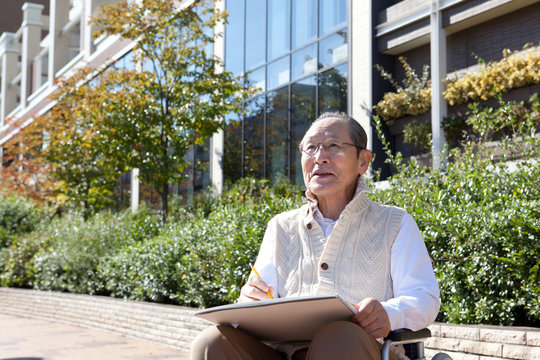 車椅子に乗って絵を描く70代男性