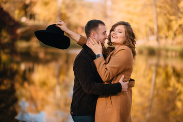 Loving man hugs his happy girlfriend on the lake in autumn park, middle-aged portrait