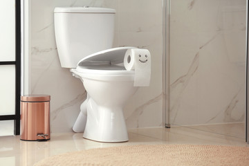 Roll of paper with funny face on toilet bowl in bathroom
