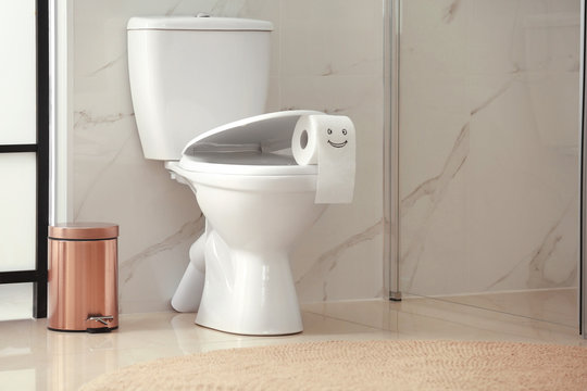 Roll Of Paper With Funny Face On Toilet Bowl In Bathroom