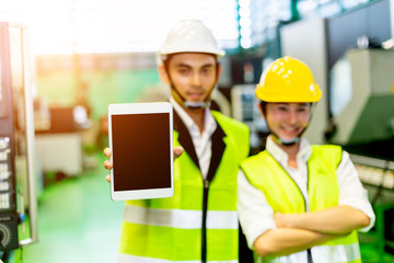 Businessmen or male engineers and female engineers are working in industrial plants that have machines and injection molds, with tablets used to control technology.