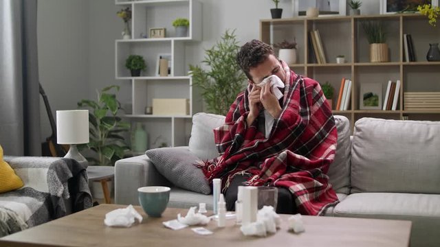 The sick man blows his nose in a napkin in the living room